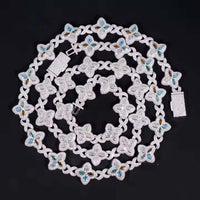 The Silver Clover Moissanite Chain, made from 925 sterling silver with flower-shaped links and blue and gold embellishments, is artfully coiled in a spiral on a black background.