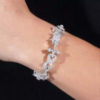 A close-up of a wrist wearing the Cross Infinity Link Moissanite Bracelet, crafted in sterling silver with cross and heart-shaped infinity links adorned with sparkling moissanite, set against a black background.