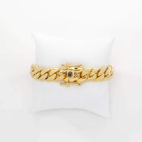 The Cuban Link Bracelet - READY TO SHIP: 9mm - 15mm Solid Gold features a crown and letter E charm, displayed on a white cushioned stand. This elegant bracelet adds a personalized touch to any look.