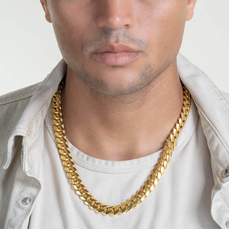A person in a light shirt and jacket wears the Cuban Link Chain 12mm - 14k Gold Bonded, with the photo focusing on their lower face, neck, and upper chest to highlight the bold necklace.
