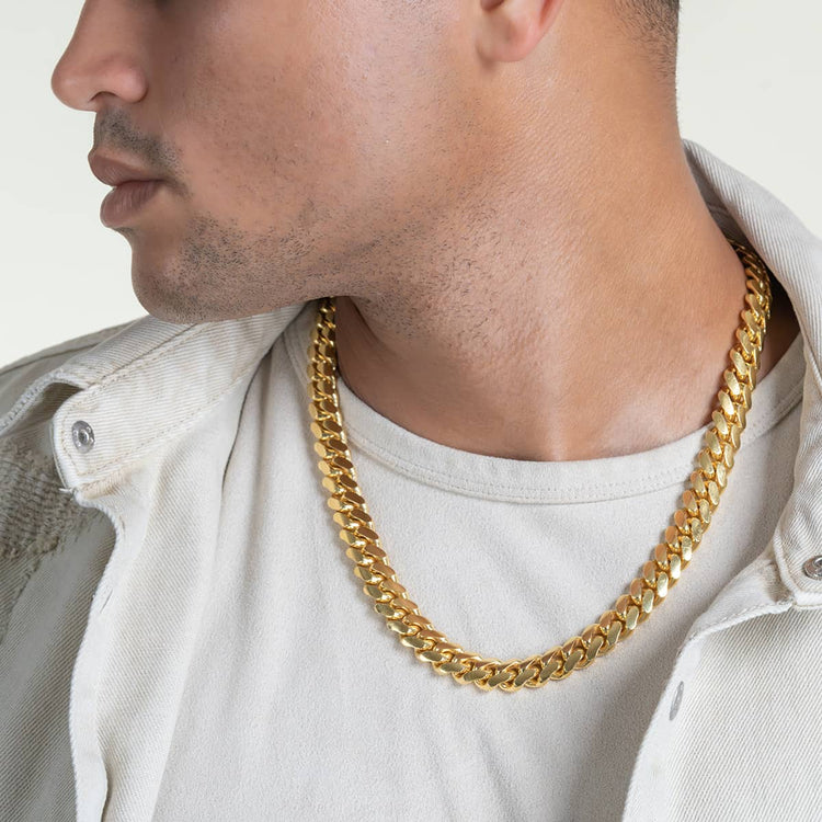 A man in a light shirt and jacket, seen from the shoulders up with his face partially turned away, showcases the Cuban Link Chain 12mm - 14k Gold Bonded around his neck.