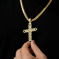A hand holds the Lab Diamond Cuban Link Cross Pendant, featuring gold and lab diamonds on a thick Cuban link chain, set against a black background.