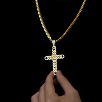 A hand holds the Lab Diamond Cuban Link Cross Pendant—a gold chain necklace with a cross-shaped pendant featuring gold links and VS Clarity lab-grown diamonds on the bail—against a black background.