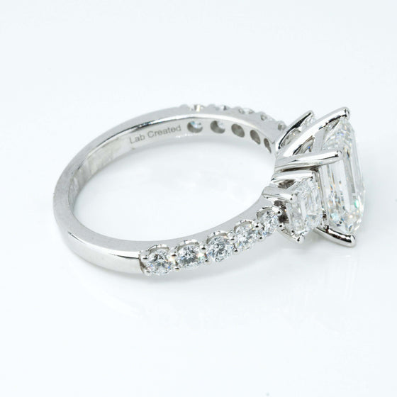 3.8 CTW 14k White Gold Three Stone Emerald Engagement Ring with emerald-cut diamond and side stones on a sleek band.