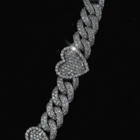 The Diamond Chain - Heart Shaped 10k White Gold features a sparkling heart-shaped charm encrusted with natural diamonds on a silver Cuban link, displayed against a black background.