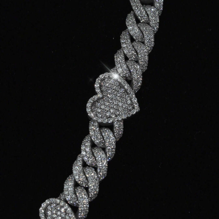 The Diamond Chain - Heart Shaped 10k White Gold features a sparkling heart-shaped charm encrusted with natural diamonds on a silver Cuban link, displayed against a black background.