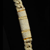 A close-up of the Diamond Cuban Link Chain - Semi Solid - 16mm showcases its 10k gold and lab-grown diamond-encrusted design, including a sparkling rectangular centerpiece, all set against a black background.