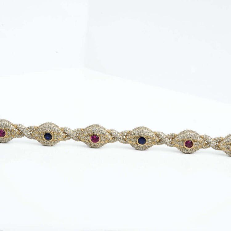 The Diamond Evil Eye Gemstone Bracelet in 10k yellow gold features alternating oval red and blue gemstones, each bordered by small natural diamonds, shown on a white background.
