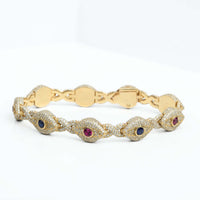 The Diamond Evil Eye Gemstone Bracelet in 10k yellow gold features natural diamonds and alternating blue and red gemstones, shown on a white surface.
