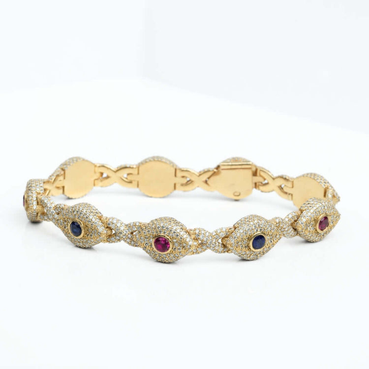 The Diamond Evil Eye Gemstone Bracelet in 10k yellow gold features natural diamonds and alternating blue and red gemstones, shown on a white surface.