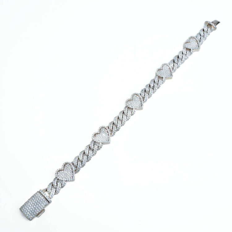 The Diamond Heart Cuban Link Bracelet showcases heart-shaped links adorned with sparkling stones and a stone-studded square clasp, set against a white background.