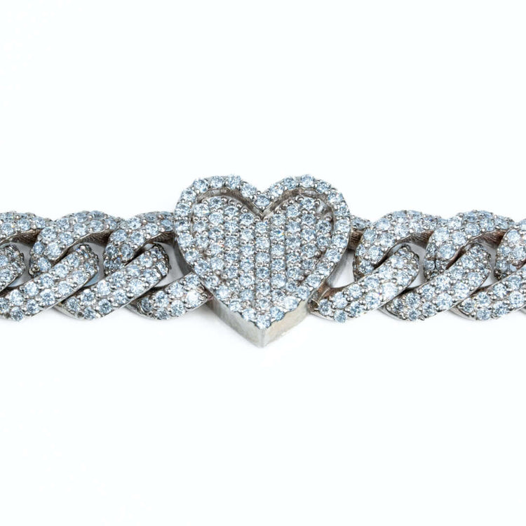 The Diamond Heart Cuban Link Bracelet features a heart-shaped pendant adorned with diamonds on a silver chain, displayed against a white background.