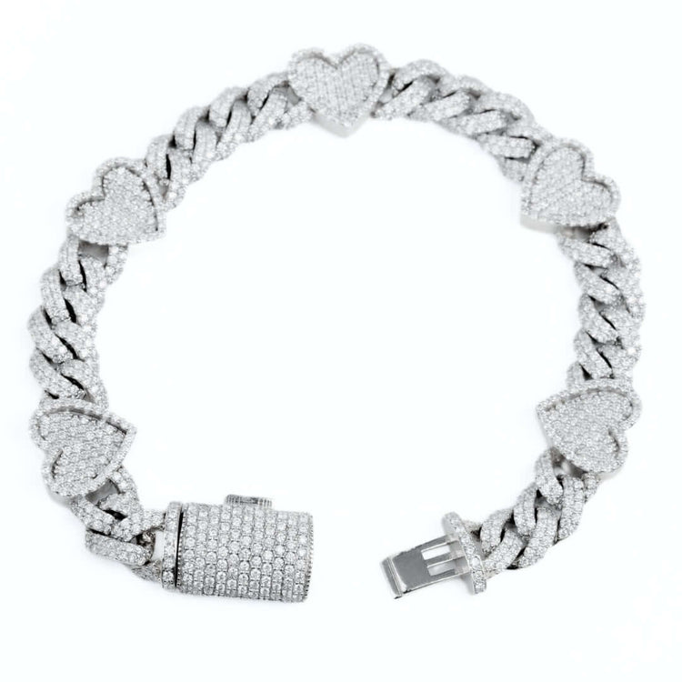The Diamond Heart Cuban Link Bracelet features thick, interlocking links and heart-shaped charms encrusted with sparkling diamonds, displayed on a white background.