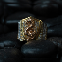The Dragon Shield Ring - 10k Solid Gold features a shield-shaped face with a raised dragon design and sparkling diamonds, elegantly set on smooth black stones.