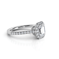 The Emerald-Cut Halo Lab Diamond Engagement Ring with Pavé Band features a lab-grown emerald-cut diamond center, surrounded by a halo of smaller diamonds on a pavé band in white gold or platinum.