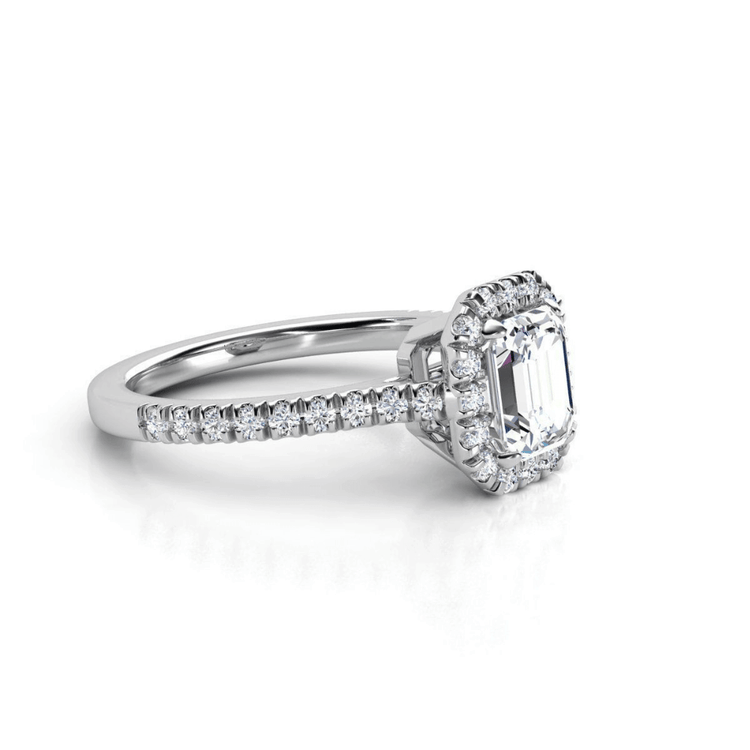 The Emerald-Cut Halo Lab Diamond Engagement Ring with Pavé Band features a lab-grown emerald-cut diamond center, surrounded by a halo of smaller diamonds on a pavé band in white gold or platinum.