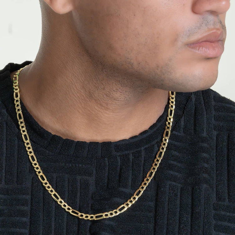 A close-up shows a person in a textured black shirt wearing the Figaro Chain 5.5mm - 14k Gold Bonded necklace, with only their lower face, neck, and upper chest visible.