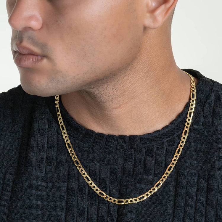A person in a black textured shirt wears the Figaro Chain 5.5mm - 14k Gold Bonded necklace, shown from the shoulders up, highlighting the men's gold chain and lower face.