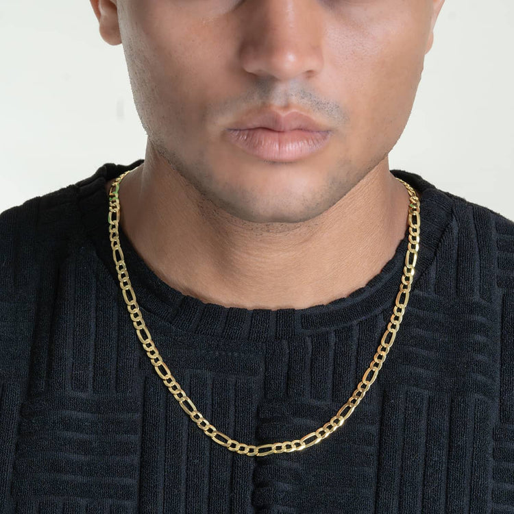 A person in a textured black shirt wears the Figaro Chain 5.5mm-14k Gold Bonded necklace, shown from the shoulders up with their face partially visible and lips closed.