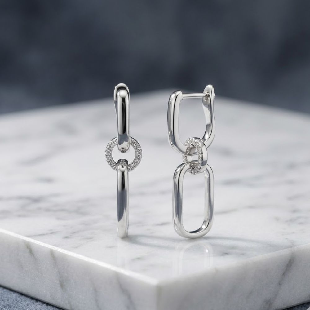 Sterling Silver Diamond Dangling Earrings 1/6CTW, featuring interlocking oval and circular links—one adorned with sparkling diamonds—are displayed upright on white marble with a blurred gray background, making them a perfect gift choice.