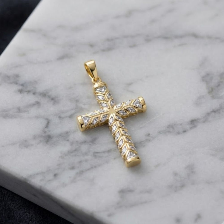 A 1/5 CTW natural diamond cross pendant in 10K gold, featuring delicate leaf-inspired patterns and sparkling natural diamonds, is displayed on a white marble surface with subtle gray veining.
