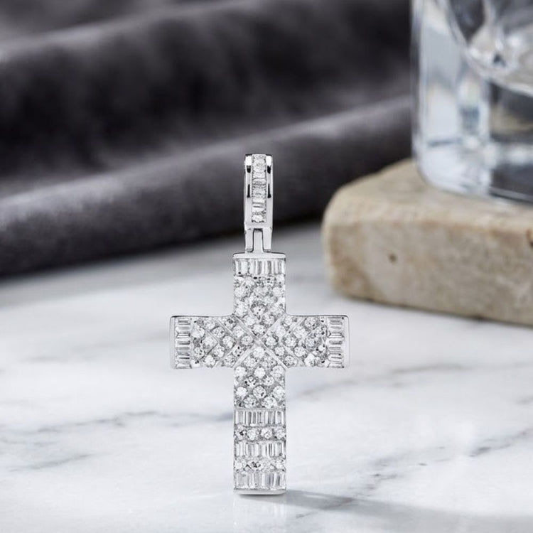 The 10K White Gold 1/2 CTW Natural Diamond Cross Pendant is beautifully showcased on a marble surface, its lustrous natural diamonds glimmering. A stone and a softly blurred glass accent the elegant background.