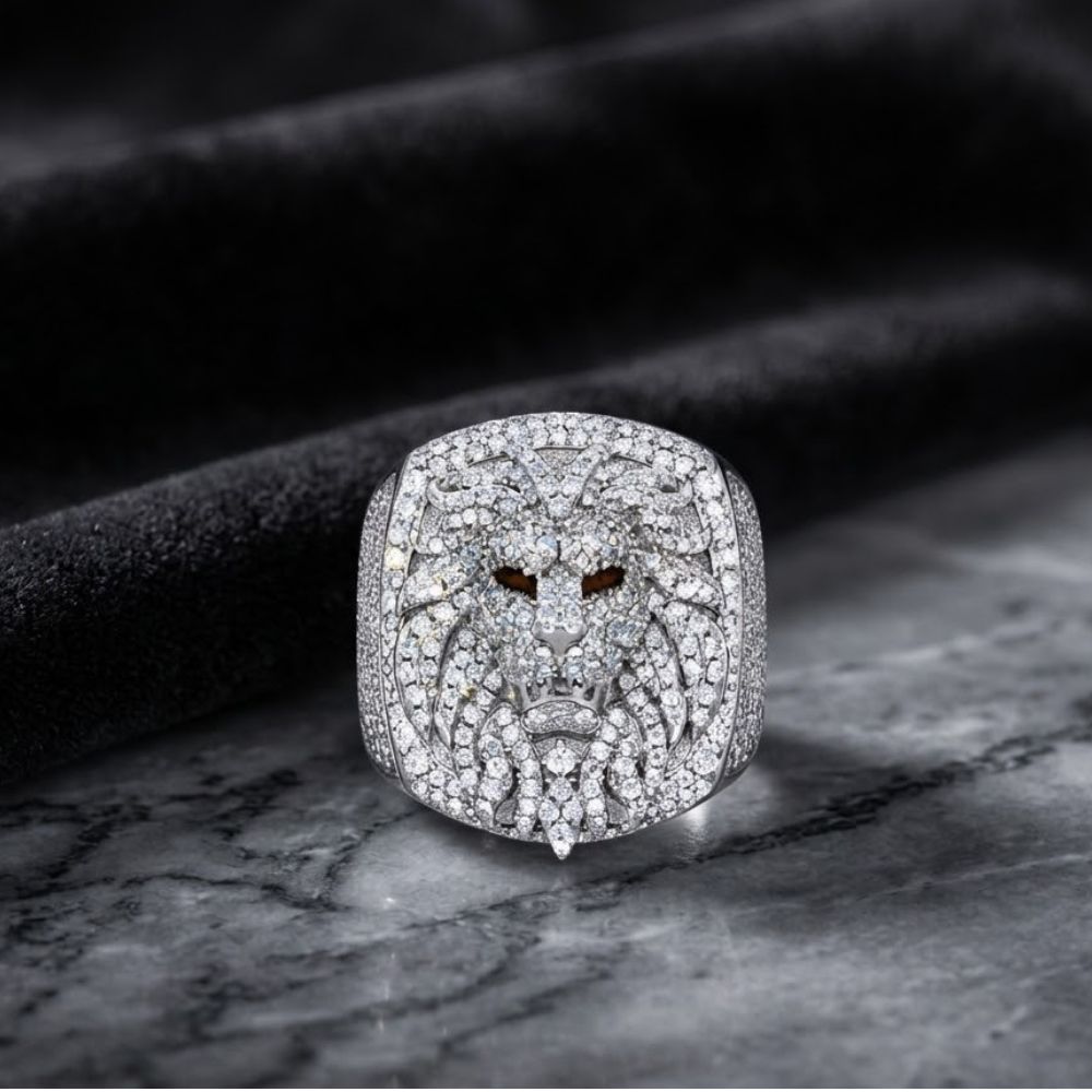 The 925 Silver Moissanite Lion Head Ring, featuring a detailed lion design and sparkling stones, is displayed on marble with a soft black backdrop—a striking piece of men’s fashion jewelry.