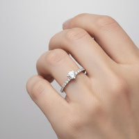 A hand wearing the Classic Solitaire Lab Diamond Ring with Dazzling Pavé Accents, featuring a brilliant round lab diamond solitaire and sparkling pavé-set stones along the band, displayed against a plain light background.
