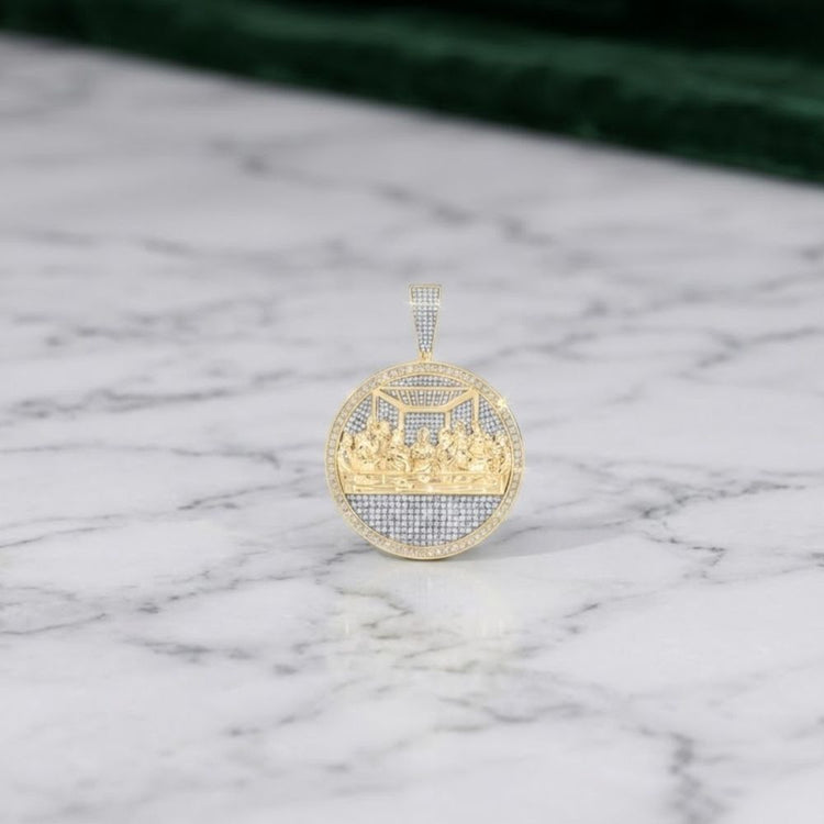 The 10k Gold 2CT Diamond Last Supper Men's Charm lies on a white marble surface, set against a green background, showcasing its detailed engraving and sparkling diamonds.