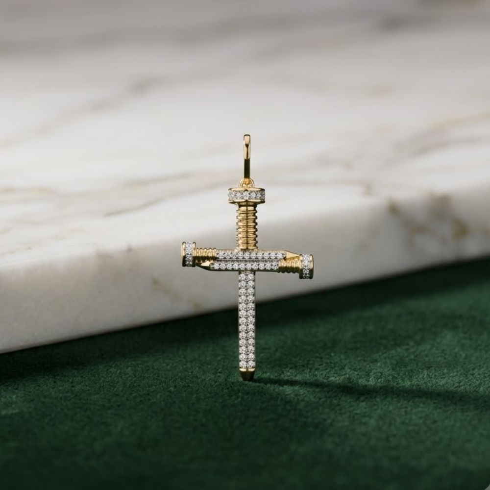 The 10K Gold Diamond Nail Cross Charm Pendant 1/3 CTW, encrusted with small diamonds, rests on a green textured surface beside a white marble slab, making a striking faith-inspired jewelry piece.