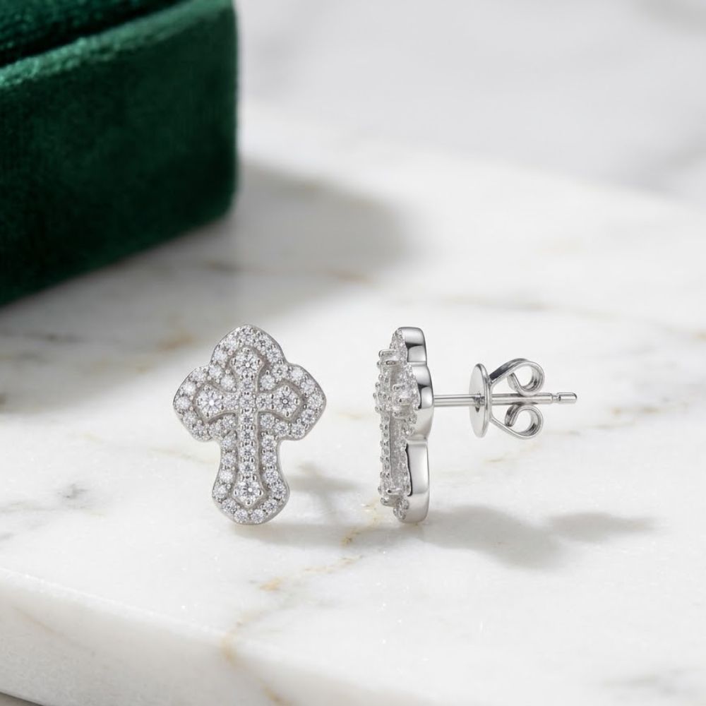 The 925 Silver Moissanite Cross Stud Earrings Unisex are displayed on white marble, with a green velvet box in the background—ideal as a stylish piece of unisex religious jewelry.