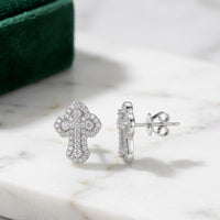 The 925 Silver Moissanite Cross Stud Earrings Unisex are displayed on white marble, with a green velvet box in the background—ideal as a stylish piece of unisex religious jewelry.