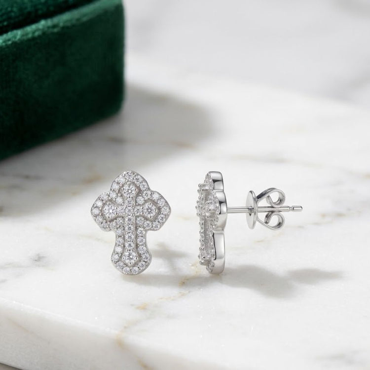 The 925 Silver Moissanite Cross Stud Earrings Unisex are displayed on white marble, with a green velvet box in the background—ideal as a stylish piece of unisex religious jewelry.