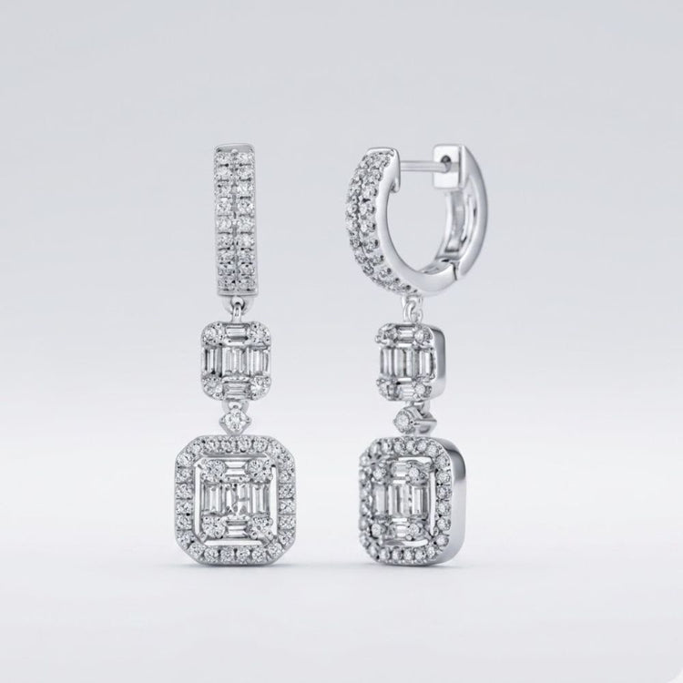 The 1 Cttw 14k White Gold Baguette Diamond Dangle Earrings feature rectangular baguette diamond clusters framed by smaller diamonds, suspended from diamond-studded hoops against a light gray background.