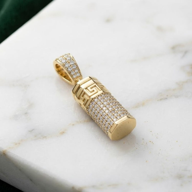 The 1CTW Diamond Urn Pendant in 10K yellow gold, featuring a Greek key pattern and encrusted with sparkling diamonds, rests elegantly on white marble—a stunning piece of memorial jewelry.