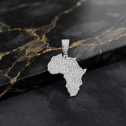 A stunning Sterling Silver Diamond Africa Pendant 1 Cttw, shaped like the African continent and adorned with shimmering diamonds, rests elegantly on a dark marble surface with gold veining.