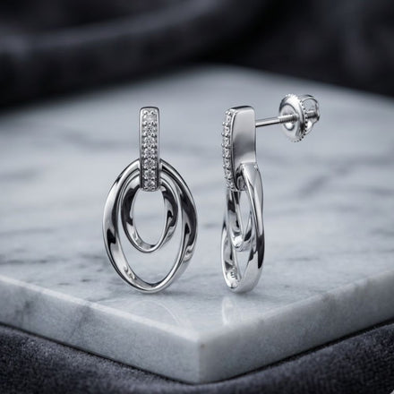 Elegant 1/12 CTW natural diamond gift earrings in sterling silver, featuring interlocking oval loops and sparkling stones, displayed on marble with a dark background—perfect for a sophisticated touch.