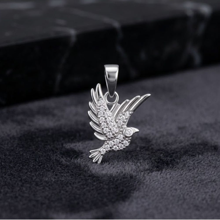 The Sterling Silver Cubic-Zirconia Peace Dove Pendant, crafted in 925 sterling silver and adorned with sparkling clear crystals, rests on a dark, textured surface against a black marble backdrop—an elegant unisex charm jewelry piece perfect for any occasion.