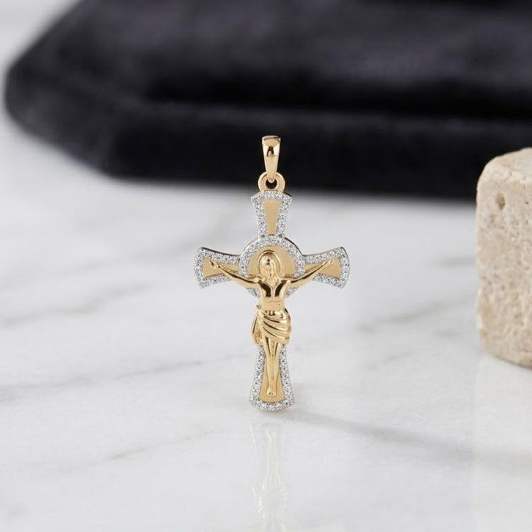 The 10K Yellow Gold 1/5 CTW Diamond Jesus Cross Pendant, featuring elegant silver accents, rests on a white marble surface with a dark cloth and beige stone in the background.