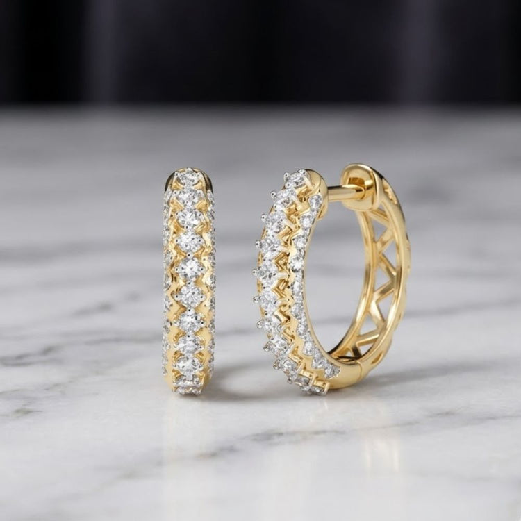 1/2 CTW Natural Diamond Hoop Earrings in 10K Gold rest elegantly on a white marble surface against a blurred dark background, highlighting the timeless beauty of 10K yellow gold and the radiant sparkle of natural diamonds.