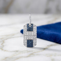 A 1-5/8CTW Diamond Dog Tag Men's Charm in 10K gold, featuring geometric patterns, stands upright on a marble surface with a folded blue cloth in the background.