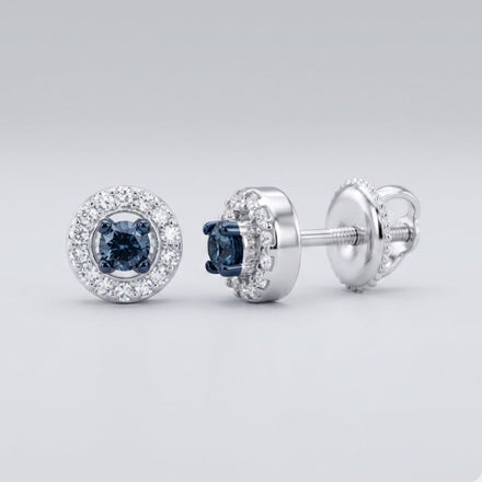 The 10k White Gold Blue Diamond Halo Earrings 1/5 Cttw showcase a central dark blue diamond framed by clear diamonds in round halos, set in white gold with screw-back posts, shown on a light gray background.