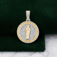 The 1 -3/4CTW St. Jude Diamond Charm in 10k gold features a detailed St. Jude center, concentric rows of natural diamonds, and a Greek key pattern, shown on green velvet with a marble background.