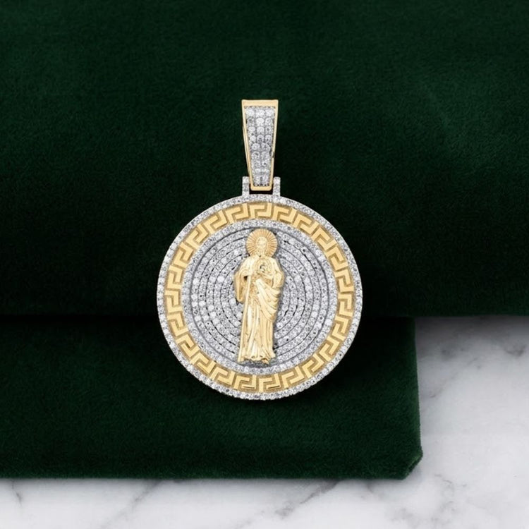 The 1 -3/4CTW St. Jude Diamond Charm in 10k gold features a detailed St. Jude center, concentric rows of natural diamonds, and a Greek key pattern, shown on green velvet with a marble background.