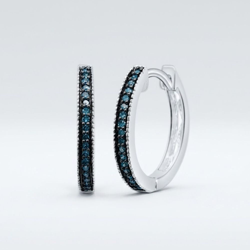 The Sterling Silver Blue Diamond Hoop Earrings 1/10 Cttw feature a single row of sparkling blue diamonds, elegantly set in sterling silver hoops and showcased against a plain light grey background.
