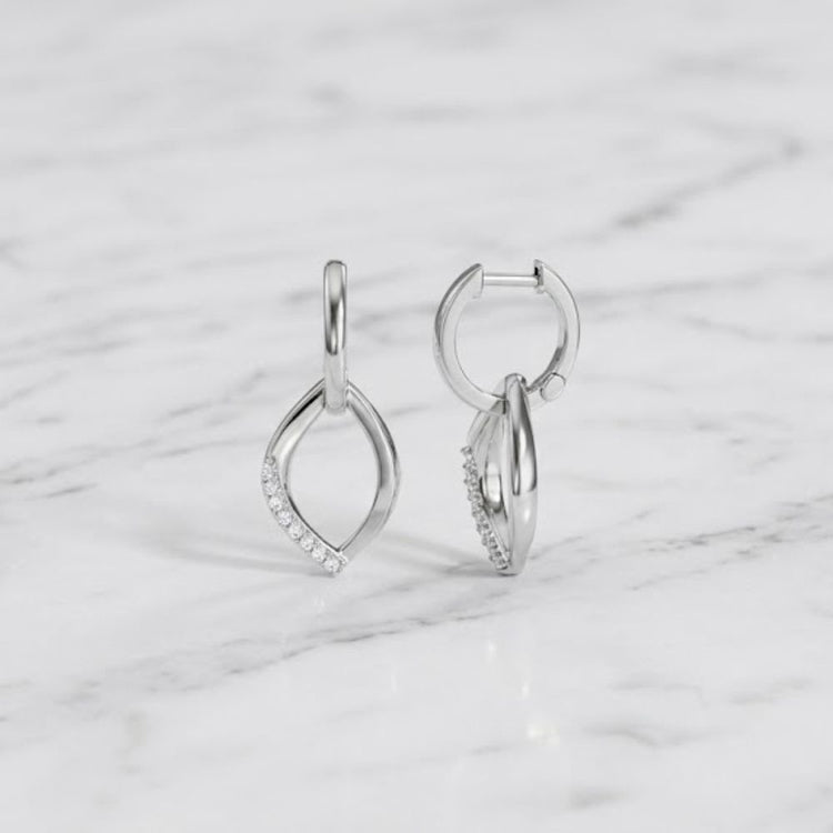 A pair of 1/8 CTW Diamond Hoop Earrings in sterling silver, featuring a leaf-shaped dangle partially encrusted with small clear stones, displayed on a white marble surface.