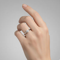 A hand with neatly manicured nails showcases the Timeless Six-Prong Solitaire Lab Diamond Ring, featuring a single round lab diamond on the ring finger against a plain gray background.