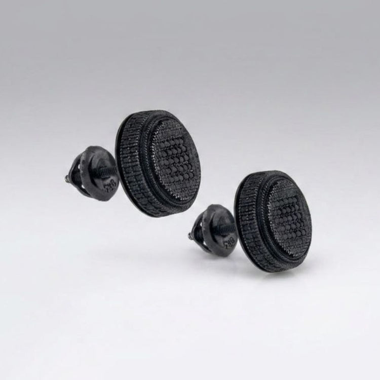 Two black objects resembling Oreo cookies sit against a gray background. On closer inspection, they are actually Black Sterling Silver Diamond Cluster Earrings with a playful, eye-catching design.