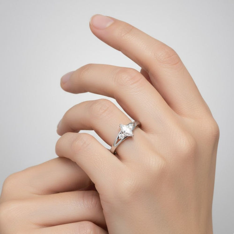 A close-up of a hand with neatly manicured nails wearing the Marquise Lab Diamond Three-Stone Engagement Ring in Platinum Finish on the ring finger, its sparkling gemstones shining brilliantly against a plain, light background.