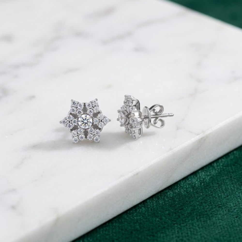 The 925 Silver Moissanite Star Stud Earrings shine on a white marble surface with a green textured background—perfect for adding sparkle to your fashion stud collection.